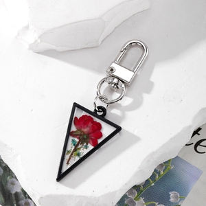 Triangle metal frame keychain with red dried rose flower inside on a white stone base
