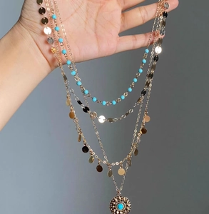 Macro detail of multi-layered gold necklace with turquoise beads and sunburst pendant