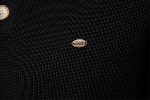 Detail of black knit fabric featuring a vintage copper button and AIOPESON metal logo