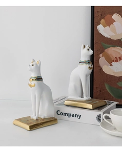 Detail of white Bastet Egyptian cat statues with golden engraved base on a bookshelf