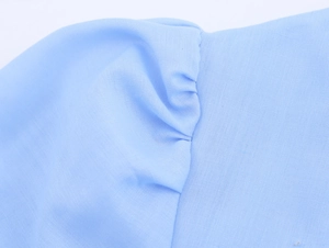 Detail of light blue embroidered dress showing textured fabric and pleated puff sleeve seams