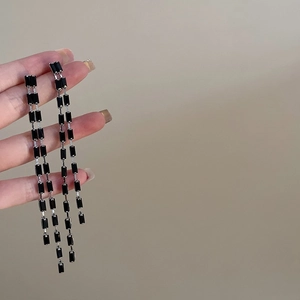 Gros plan de longues boucles d'oreilles à pompons en perles noires rectangulaires