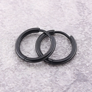 Close-up of matte black stainless steel hoop earrings on a textured stone surface