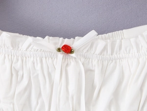 Détail de la taille à volants blancs avec une rose rouge et un nœud sur coton