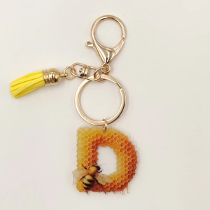Detail of Letter D acrylic keychain with honey bee pattern, gold clasp and yellow tassel
