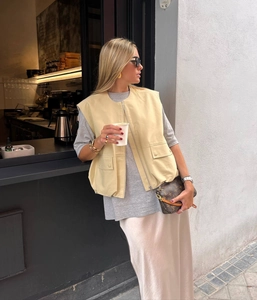 Detail view of beige zip-up vest with pleated hem on a model in an urban street setting