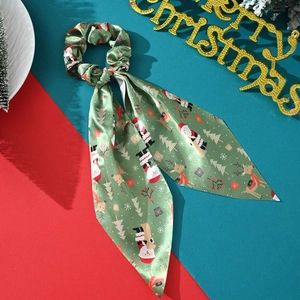 Detail view of a green satin Christmas scrunchie with ribbons and holiday patterns