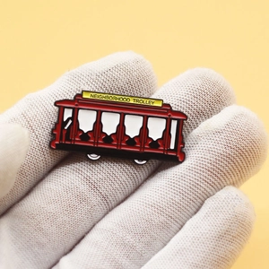 Macro shot of Neighborhood Trolley enamel pin in red held by a gloved hand