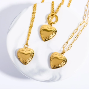 Three gold heart locket necklaces with scroll engraving on white marble base