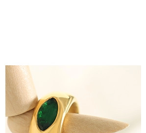 Detail of a polished gold ring featuring a marquise-cut green gemstone on a wooden model