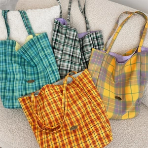 Close-up of four colorful plaid canvas tote bags stacked on soft white textured fabric
