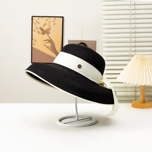 Detailed texture of black woven straw hat with white ribbon and metal M logo