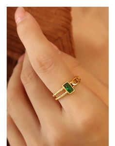 Détail d'une bague dorée avec zircon émeraude, texture corde et éléments de chaîne