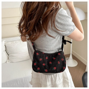 Black corduroy shoulder bag with red strawberry pattern shown on a female model