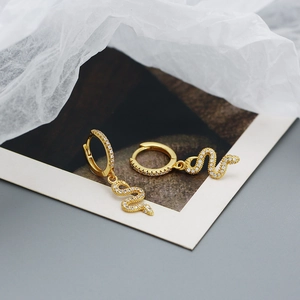 Detailed view of gold snake earrings with white zirconia pave on textured artistic paper