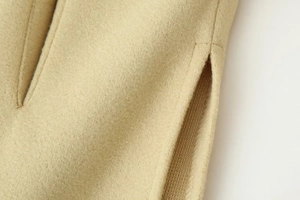 Macro detail of camel wool coat showing premium fabric texture and side slit stitching