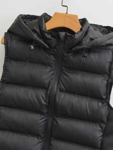 Detail of black hooded puffer vest with quilted texture on wooden hanger against white wall