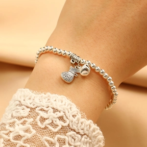 Close-up of silver beaded bracelet with fortune bag and small bell charm on lace cuff