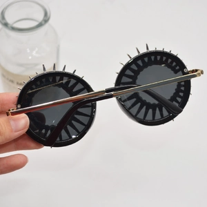 Retro round sunglasses with black frames and gold punk spikes shown in hand closeup