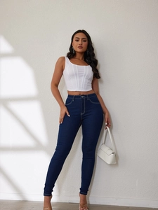 Detail view of high-waist slim fit jeans in dark blue paired with a white tank top