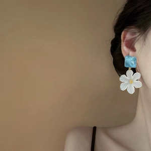 Detailed view of elegant blue acrylic and white flower pendant earrings on a model