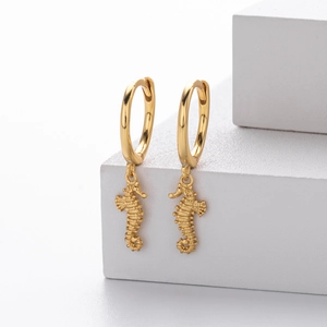 Detailed close-up of golden seahorse charm earrings displayed on white geometric blocks