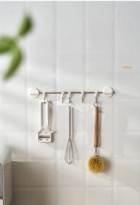 Detail of adjustable five-hook wall rack holding kitchen utensils on white tile wall