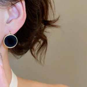 Detail of round black velvet earring with gold trim worn by model in soft lighting