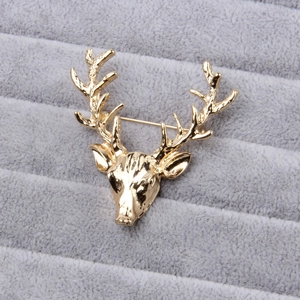 Detailed close-up of a vintage golden elk head brooch on a textured grey fabric background