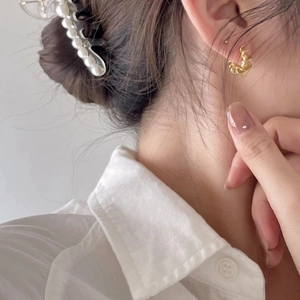 Close-up of golden twist hoop earrings and pearl hair clip on a model with white shirt