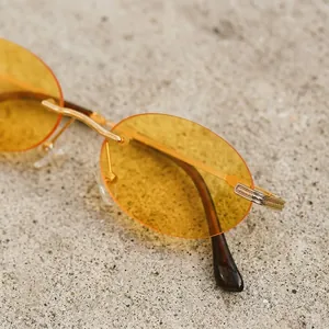 Frameless oval sunglasses with amber lenses and gold metal bridge on stone surface