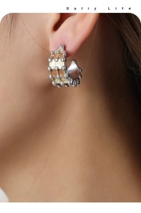 Macro side view of silver C-shaped earrings with brown plaid enamel on a female model