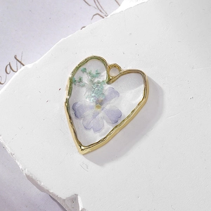 Macro shot of heart-shaped resin pendant with real purple flowers and gold alloy frame
