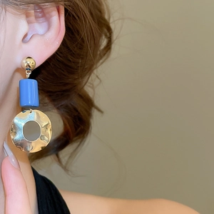 Close-up of model wearing geometric drop earrings with blue bead and hammered gold disc