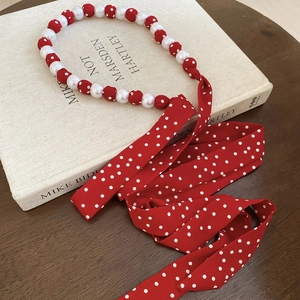 Detail of red polka dot silk scarf necklace with elegant white pearls on vintage book