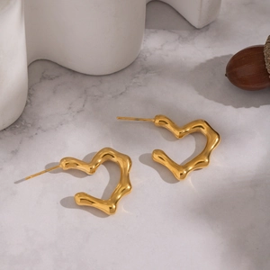 Detail of wavy heart earrings in gold finish on elegant marble surface display