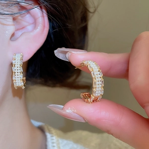 Detail of gold C-shape earrings with inlaid pearls and rectangular zircons