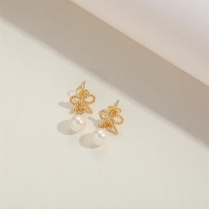 Close-up detail of golden bow earrings with pearl pendants on a neutral surface