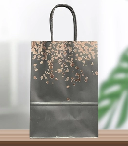 Detail of black kraft gift bag featuring metallic rose gold heart patterns and rope handles