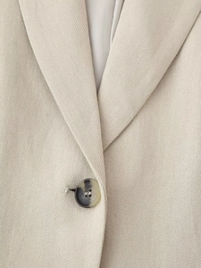 Detailed close-up of beige blazer fabric texture with dark tortoiseshell button detail