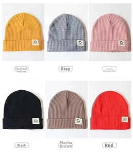 Detail view of ribbed knit baby beanies featuring smiley face patches in six vibrant colors