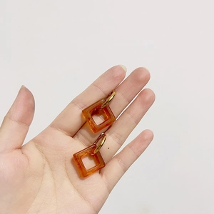 Close-up of amber resin square earring with gold metal clasp held in hand