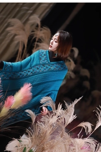 Close-up of blue knitted poncho with diamond patterns and tassel fringe details