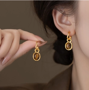 Detailed close-up of gold-plated oval tiger eye stone earrings on model ear