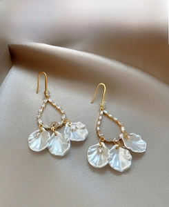 Détail de boucles d'oreilles coquillages dorés avec strass sur tissu en soie beige