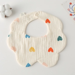 Detail of petal-shaped cotton gauze baby bib with colorful heart prints and soft texture