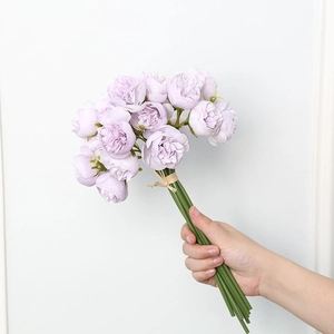 Hand-held artificial lavender peony bouquet tied with hemp rope against a white wall