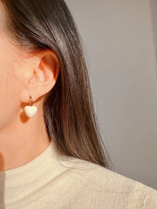 Detailed view of handmade cream heart earrings with gold hoops worn by a model