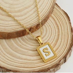 Close-up of 18K gold stainless steel S-letter shell pendant on wooden coasters