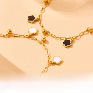 Detail of gold chain bracelet with black and white shell clover pendants and beads